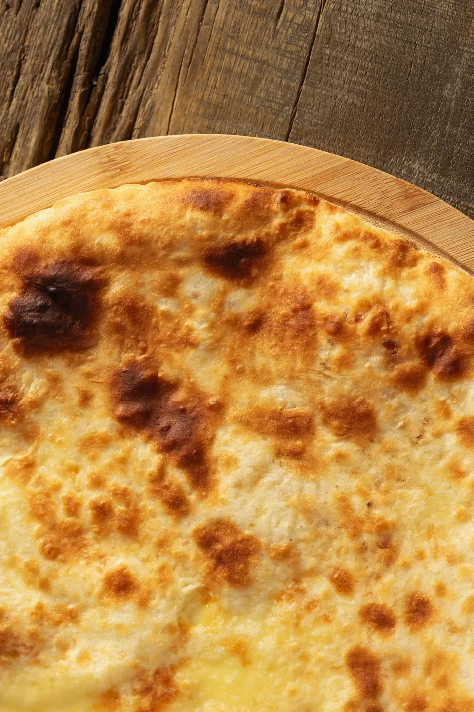 Close-up of a round browned cheese bread on a wooden board